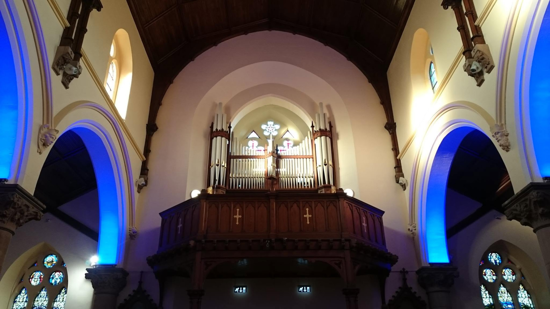 A rebuilt gallery organ lit in blue and gold beneath the chancel arch